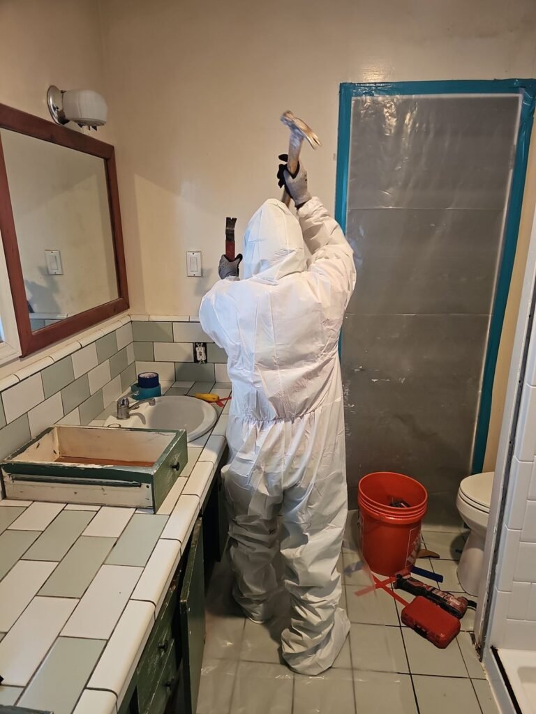 A technician spraying in a bathroom with the shower sealed behind plastic in the East Bay