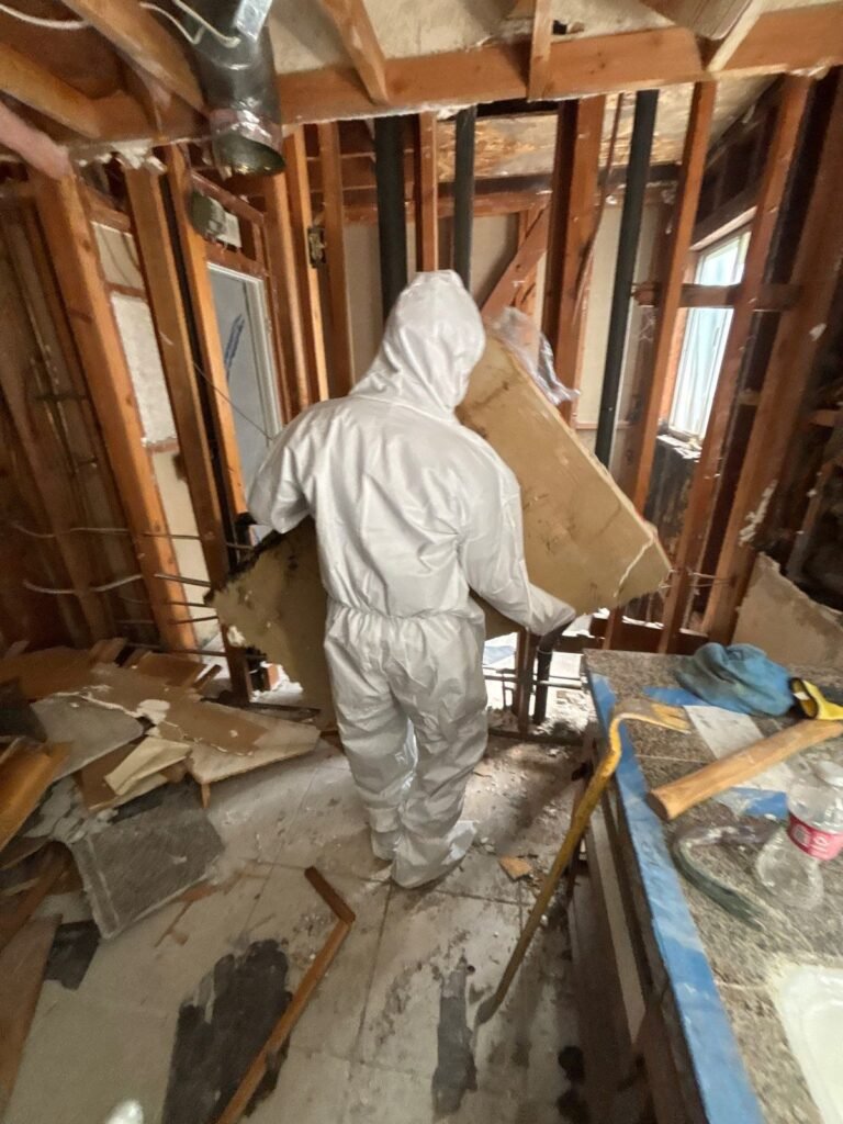 A technician carrying debris out of a room stripped to the studs in the East Bay