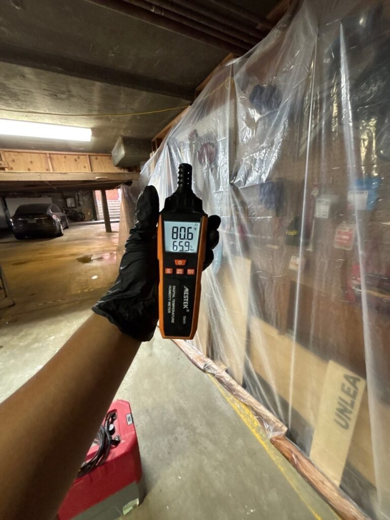 A gloved hand holding a humidity meter beside containment plastic in a crawl space in the East Bay