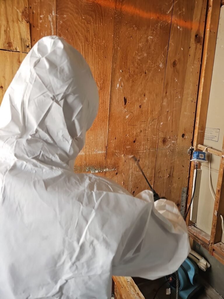 A hooded technician beside an old board wall with equipment at floor level in the East Bay