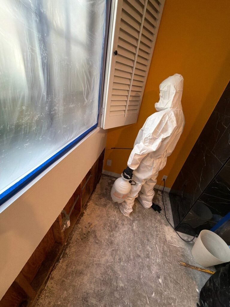 A technician crouched beside an orange wall with the baseboard removed in the East Bay