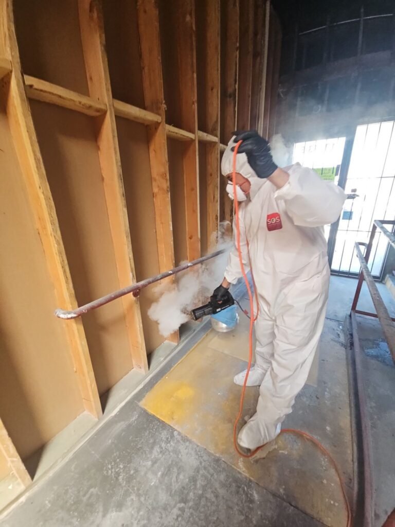 A technician in a full suit spraying an open wall stripped to the studs in the East Bay